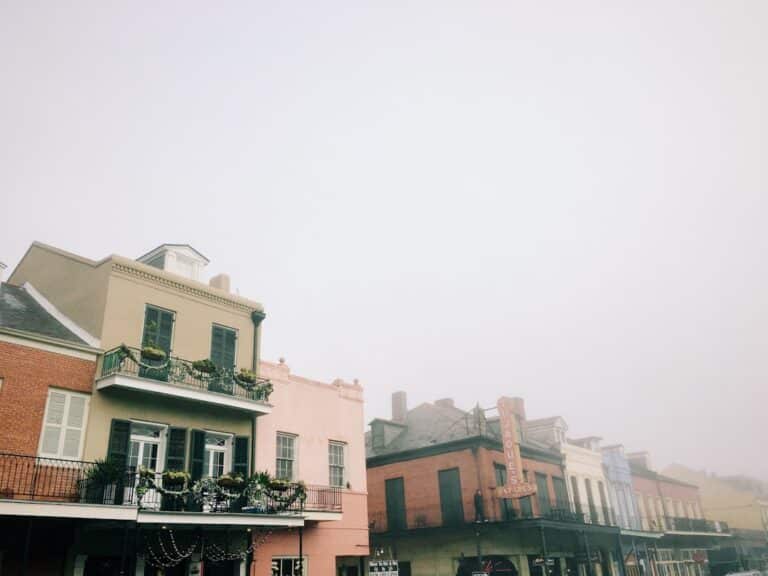 Professional photograph of a classic New Orleans street with gas lamps and balconies disappearing into a thick morning fog...