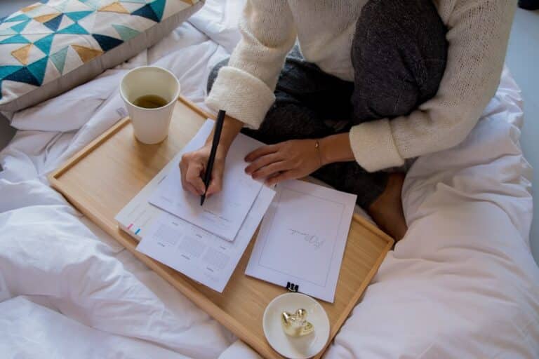 Young couple sits at a bright, modern dining table, looking thoughtfully over papers that could be mortgage documents or h...