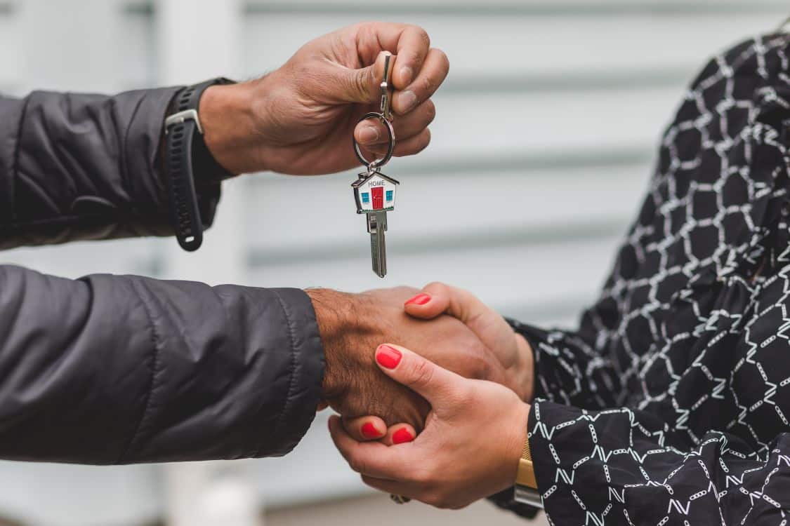 A person's hand holding a house key poised to unlock the front door of a beautiful, modern home, symbolizing a successful and smart financial outcome.