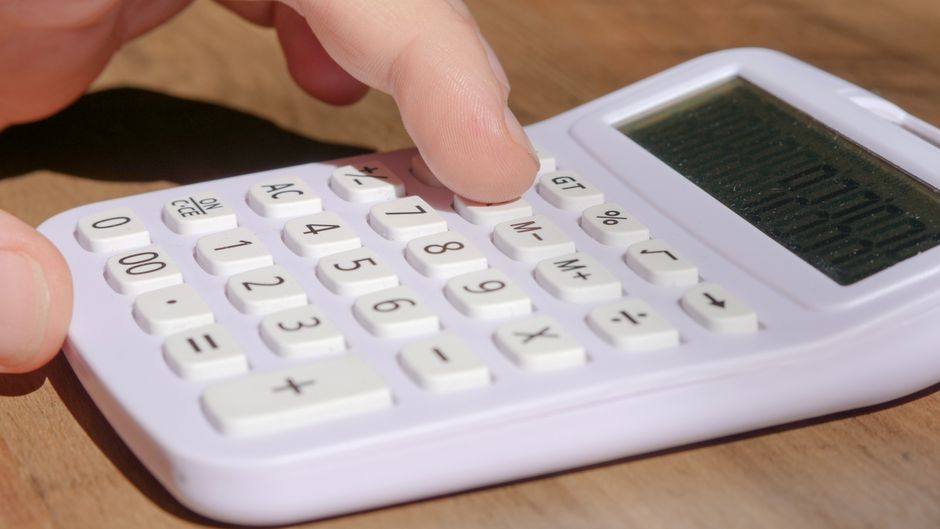 A calculator and a set of house keys resting on a clean, modern desk, symbolizing the financial planning and savings involved in selling a home with a flat-fee or 1% commission model.