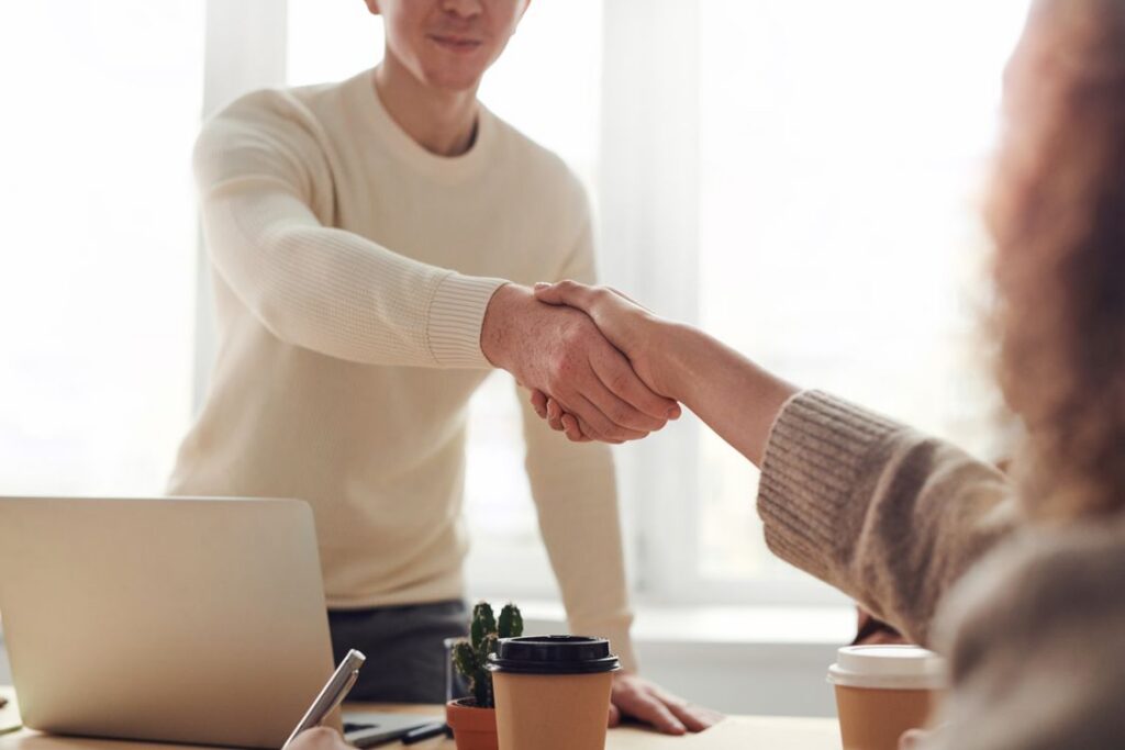 Two professional real estate agents, a man and a woman, shaking hands in agreement in front of a beautiful modern suburban...