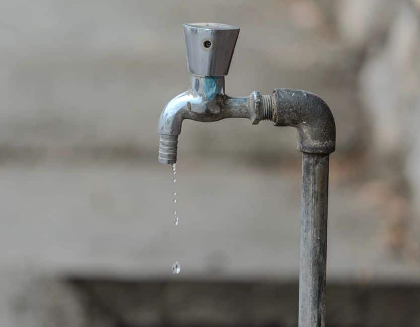 A close-up shot of a single water droplet falling from a sleek, chrome kitchen faucet, illustrating the concept of home equity slowly and silently draining away.