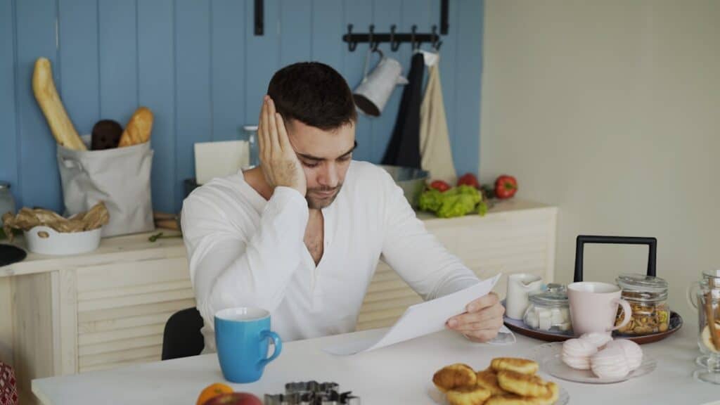 Concerned couple sits at their dining room table, carefully reviewing financial documents related to their home sale, illu...
