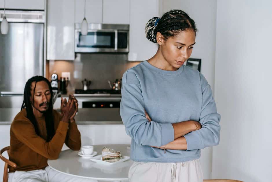 Homeowner sits at their modern kitchen table, looking concerned at a stack of papers and a calculator, representing the fi...
