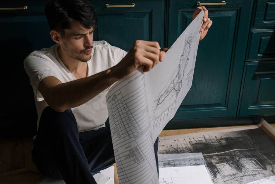 Homeowner thoughtfully reviews architectural blueprints on a wooden table, planning strategic home improvements for a succ...