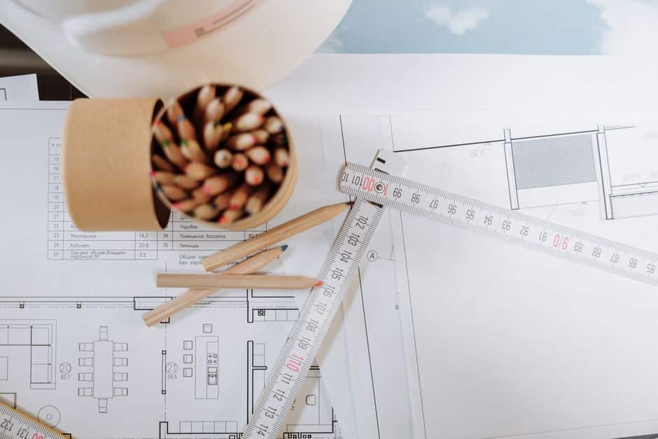 An old, yellowed architectural blueprint is spread across a clean, modern desk with a laptop, symbolizing the use of outdated home comps in today's market.