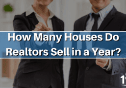 Two realtors, one holding a small model home and one holding keys, representing a home sale.