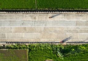 Aerial drone shot of a major new highway interchange under construction on a bright, sunny day, symbolizing large-scale in...