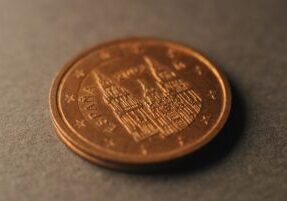 Hand carefully placing a single coin onto a miniature house, symbolizing real estate commission savings.