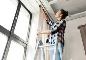 Home-improvement--decoration-and-renovation-concept---happy-smiling-woman-on-ladder-hanging-curtains--woman-on-ladder-hang...