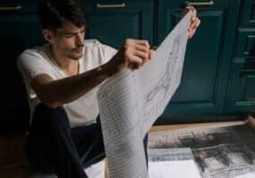 Homeowner thoughtfully reviews architectural blueprints on a wooden table, planning strategic home improvements for a succ...