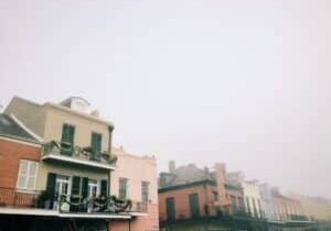 Professional photograph of a classic New Orleans street with gas lamps and balconies disappearing into a thick morning fog...