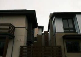 Side-by-side view of two distinct, modern suburban homes under a bright, clear sky, representing a choice in real estate s...