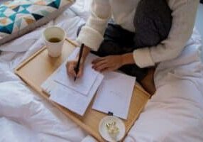 Young couple sits at a bright, modern dining table, looking thoughtfully over papers that could be mortgage documents or h...